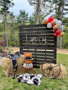 a wooden sign with balloons and hay bales in the grass next to a chair