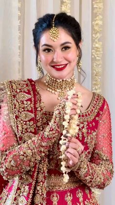 a woman in a red and gold bridal outfit holding a white flower garland on her head