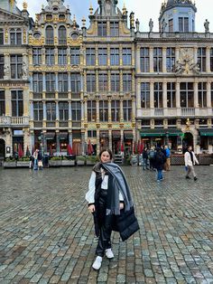 a woman is standing in the middle of a cobblestone street with buildings behind her