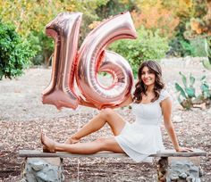 a woman is sitting on a bench with balloons in the shape of the number sixteen