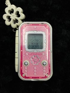 a pink and white electronic device sitting on top of a black surface next to a keychain