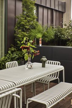 a white table and chairs on a wooden deck with green plants in the back ground