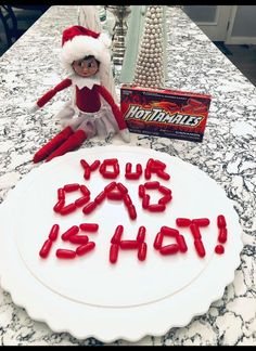 a birthday cake with the message'your dad is hot'on it and an elf doll next to it