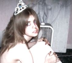 a woman wearing a tiara sitting on top of a bed next to a fan