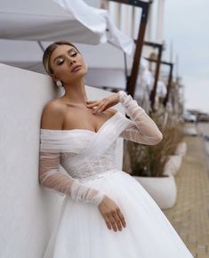 a woman in a white dress leaning against a wall with her hand on her shoulder