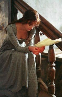 a woman sitting on top of a wooden stair case holding a piece of paper in her hand