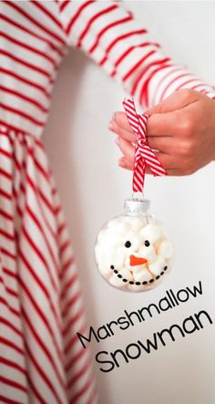 a person holding a snowman ornament in front of a red and white striped shirt