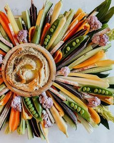 an arrangement of different vegetables arranged in a circular arrangement on a white surface with green and orange flowers