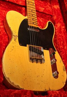 an old yellow guitar sitting on top of a red cloth