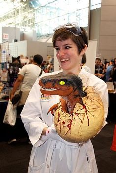 a woman is holding a fake dinosaur in her hand and wearing a white lab coat