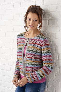 a woman leaning against a white brick wall wearing a colorful crochet cardigan