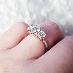 a close up of a person's hand holding a ring with three diamonds on it