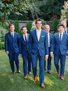 a group of men in blue suits standing next to each other on top of a lush green field