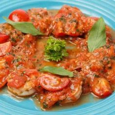 a blue plate topped with shrimp covered in tomato sauce and garnished with green leaves