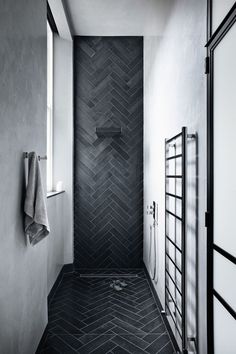 a black and white photo of a bathroom with herringbone tile on the floor, shower curtain, towel rack, and window