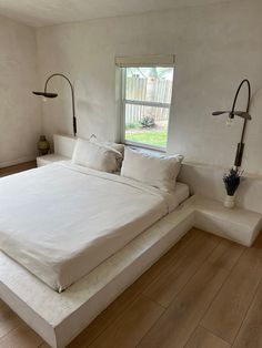 a large white bed sitting in a bedroom next to a window with two lamps on each side