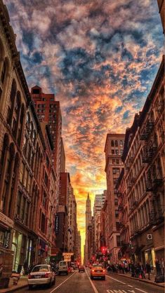 a city street filled with tall buildings under a colorful sky at sunset or sunrise in new york city