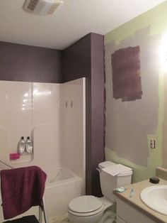 a white toilet sitting next to a bath tub under a bathroom mirror with purple paint on the walls