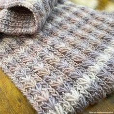 a gray and white knitted blanket laying on top of a wooden table