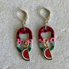 two pairs of earrings with watermelon slices hanging from hooks on carpeted surface