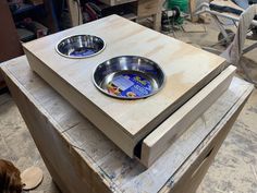 two metal bowls sitting on top of a wooden table next to a brown dog bowl