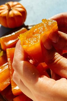 a person is peeling an orange slice into small pieces on a cutting board next to some pumpkins