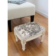 a white foot stool sitting on top of a hard wood floor next to a book