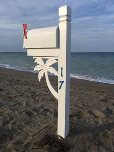 a white mailbox sitting on top of a sandy beach next to the ocean with a palm tree