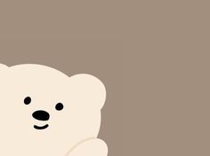 a white teddy bear sitting in front of a brown wall