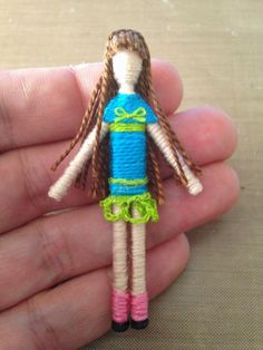 a hand holding a small doll with long hair and green dress on it's body