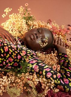 a woman laying on the ground with flowers all around her and looking at the camera