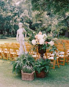 an outdoor ceremony setup with chairs, flowers and a statue in the center surrounded by greenery