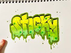 someone is drawing graffiti on paper with green and yellow ink, while holding a pen in their left hand