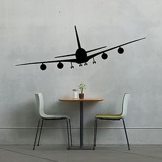 an airplane flying over a table with two chairs in front of it and the wall is painted white