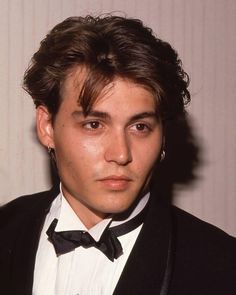 a young man in a tuxedo and bow tie looks at the camera while wearing earrings