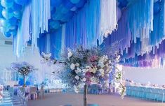 a room with blue and white balloons hanging from the ceiling, tables set up for an event