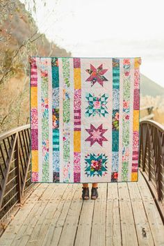 a woman holding up a colorful quilt on a bridge