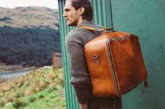 a man with a brown bag standing next to a green wall and looking off into the distance