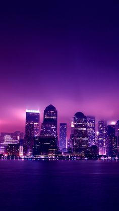 the city skyline is lit up at night with purple hues in the sky and water