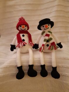 two knitted snowmen standing next to each other on a white blanket with black feet