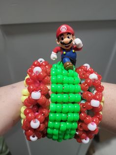 a person is holding up a bracelet made out of balloons and mario bros character beads