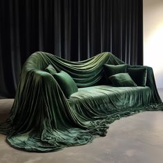 a couch covered in green fabric sitting on top of a floor next to a black curtain