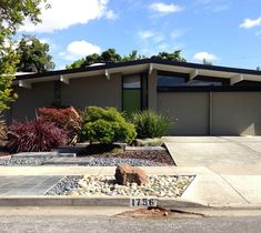 a modern house with landscaping and rocks in the front yard, on a sunny day