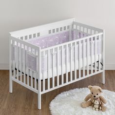 a white crib with a teddy bear sitting on the floor in front of it