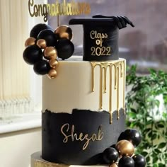 a three tiered cake with black and gold decorations on the top is decorated with balloons