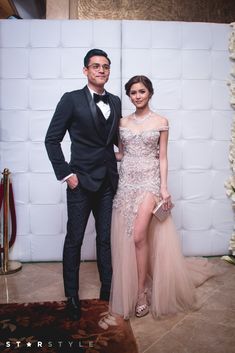 a man and woman standing next to each other in front of a white wall with flowers