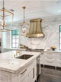 a large kitchen with marble counter tops and white cabinets, gold pendants hanging from the ceiling