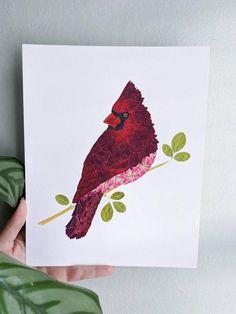 a hand holding up a card with a red bird on it's back and green leaves in the background