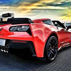 a red sports car is parked in front of some other cars on the street at sunset