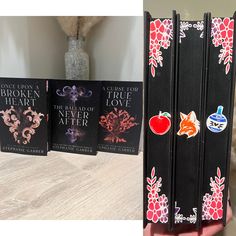 three books with designs on them sitting on a table next to a vase filled with flowers